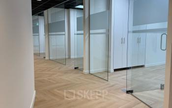 Moderne kantoorruimte huren op Hoedemakerplein 2 in Enschede met glazen wanden en houten vloer, ideaal voor zakelijke activiteiten.