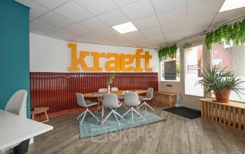 Moderne en ingerichte kantoorruimte aan de Boddenkampsingel 95 in Enschede met tafels, stoelen en planten. Grote oranje letters op de achtergrond en een comfortabele werkplek voor het huren van kantoren.