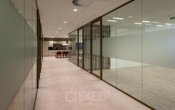 Moderne kantoorruimte op Kuipersdijk 2-4 in Enschede met glazen wanden en zicht op een gemeubileerde vergaderruimte. Ideaal voor bedrijven die kantoorruimte willen huren.