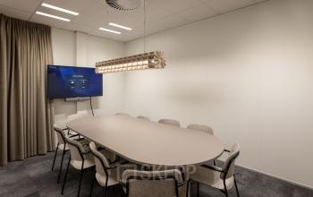 Moderne vergaderruimte in het kantoorpand op Kuipersdijk 2-4, Enschede, met een lange tafel omringd door stoelen en een digitale presentatiescherm. Ideaal voor bedrijven die kantoorruimte willen huren.