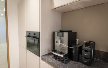 Moderne kitchenette in een kantoorpand op Kuipersdijk 2-4, Enschede, voorzien van een hoogwaardige koffiemachine en opbergmogelijkheden.