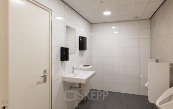 Kantoorruimte huren aan Kuipersdijk 2-4 in Enschede met een nette toiletruimte voorzien van witte tegels, wastafel en urinoirs. Ideaal voor kantoorpand dat hygiëne hoog in het vaandel heeft.