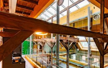 Kantoorruimte huren op Prins Hendrikkade 3 in Franeker, met houten balken, glazen wanden en een open lichtkoepel. Industriële inrichting met tapijtvloer in multifunctioneel kantoorpand.