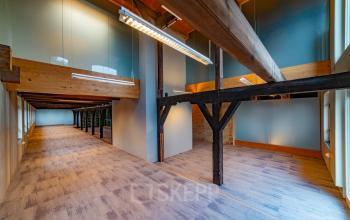 Kantoorruimte huren op Prins Hendrikkade 3, Franeker met een ruimtelijk interieur en houten balken. De ruimte oogt licht dankzij grote ramen en moderne verlichting, geschikt voor diverse kantooropstellingen.
