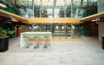 Moderne kantoorruimte huren op Prins Hendrikkade 3 in Franeker, met hoge plafonds, glazen elementen en comfortabele zitplaatsen aan een witte hoge tafel in het kantoorpand.
