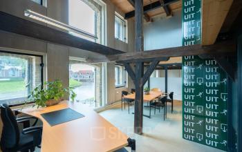 Kantoorruimte op de eerste verdieping van een kantoorpand aan Prins Hendrikkade 3 in Franeker, voorzien van houten balken, grote ramen, en diverse werkplekken met bureaus en stoelen.
