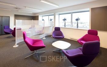 Kantoorruimte huren in Geleen met moderne paarse stoelen en bijzettafels, natuurlijk licht door grote ramen, ideaal voor een ontspannen werkomgeving.