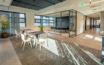 Moderne kantoorruimte met glazen wanden, voorzien van tafels en stoelen, natuurlijk licht via grote ramen voor het huren van kantoorruimte in Gouda, Tielweg 30.