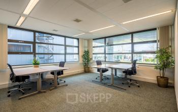 Kantoorruimte huren op Tielweg 30, Gouda met twee bureaus bij grote ramen en veel lichtinval. Moderne inrichting met planten, geschikt voor flexibel werken.