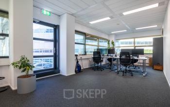 Heldere kantoorruimte met vier bureaus, stoelen en een plant in een kantoorpand op Groningenweg 8 8 in Gouda. Grote ramen zorgen voor veel licht. Ideaal voor wie kantoorruimte wil huren.