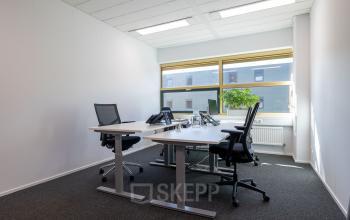 Verlichte kantoorruimte in Gouda met vier bureaustoelen en een groot raam, ideaal om te huren voor efficiënte werkplekken.