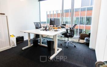 Modern kantoorruimte huren in Gouda met grote ramen, twee bureaus, bureaustoelen, en computers, ideaal voor professioneel werken.