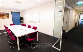Kantoorruimte huren in Gouda aan Kampenringweg 45 met een moderne vergaderruimte voorzien van roze stoelen rond een witte tafel, ideaal voor zakelijke bijeenkomsten.