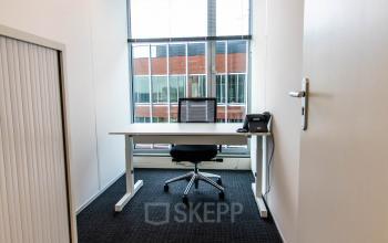 Compacte kantoorruimte huren in Gouda met een strak bureau, bureaustoel en telefoon bij het raam op Kampenringweg 45.