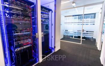 Kantoorruimte huren in Gouda met zicht op moderne serverkasten en een vergaderruimte in de achtergrond. Het kantoorpand biedt een professionele omgeving voor diverse zakelijke activiteiten.