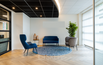 Gezellige ontvangstruimte in het kantoorpand aan Atoomweg 6B, Groningen, met moderne stoelen en een blauw tapijt, perfect voor informele gesprekken of wachtende bezoekers. Er zijn geen mensen aanwezig.