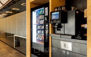 Kantoorruimte huren aan de Atoomweg 6B in Groningen met moderne voorzieningen zoals een koffiezetapparaat en een automaat voor snacks. Een glazen wand scheidt twee gedeelten van het interieur.