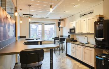 Kantoorpand aan de Leonard Springerlaan 7 in Groningen met een moderne pantry. De ruimte is voorzien van hoge tafels en stoelen, een koffieautomaat en biedt uitzicht op de stad.