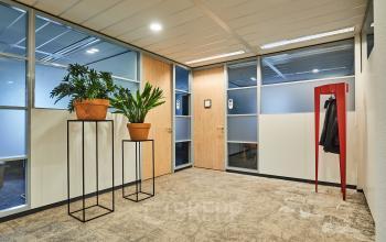 Binnenkant van een kantoorpand op Leonard Springerlaan 7, Groningen, met planten op standaards en een rode kapstok naast een deur. Ideaal voor wie kantoorruimte wil huren.