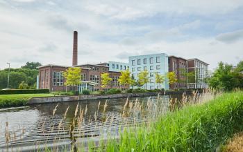 Uitzicht op het kantoorpand aan de Friesestraatweg 207-221 in Groningen, gelegen aan het water met een klassieke bakstenen gevel en hoge ramen.
