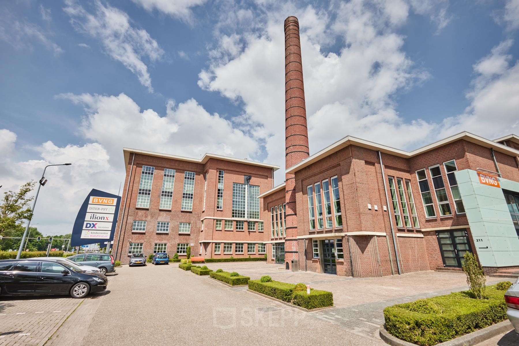 Exterieur van het kantoorpand op Friesestraatweg 207-221 in Groningen, met bakstenen gevels en hoge schoorsteen, ideaal voor kantoorruimte huren.