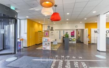 Entree van een modern kantoorpand op Zernikepark 12, Groningen, met kleurrijke lampen en een ontvangstruimte. Ideaal voor kantoorruimte huren. Verschillende folders en aanwijzingen voor bezoekers zijn zichtbaar.