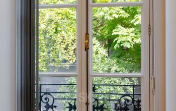 Uitzicht door een groot raam met smeedijzeren balkon, groene bomen buiten. Ideaal voor kantoorruimte huren in Haarlem Centraal Station, Kennemerplein 20.