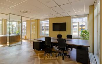 Moderne kantoorruimte te huur op Kennemerplein 20 in Haarlem Centraal Station met grote vergadertafel, stoelen en glazen wanden, ideaal voor zakelijke bijeenkomsten.