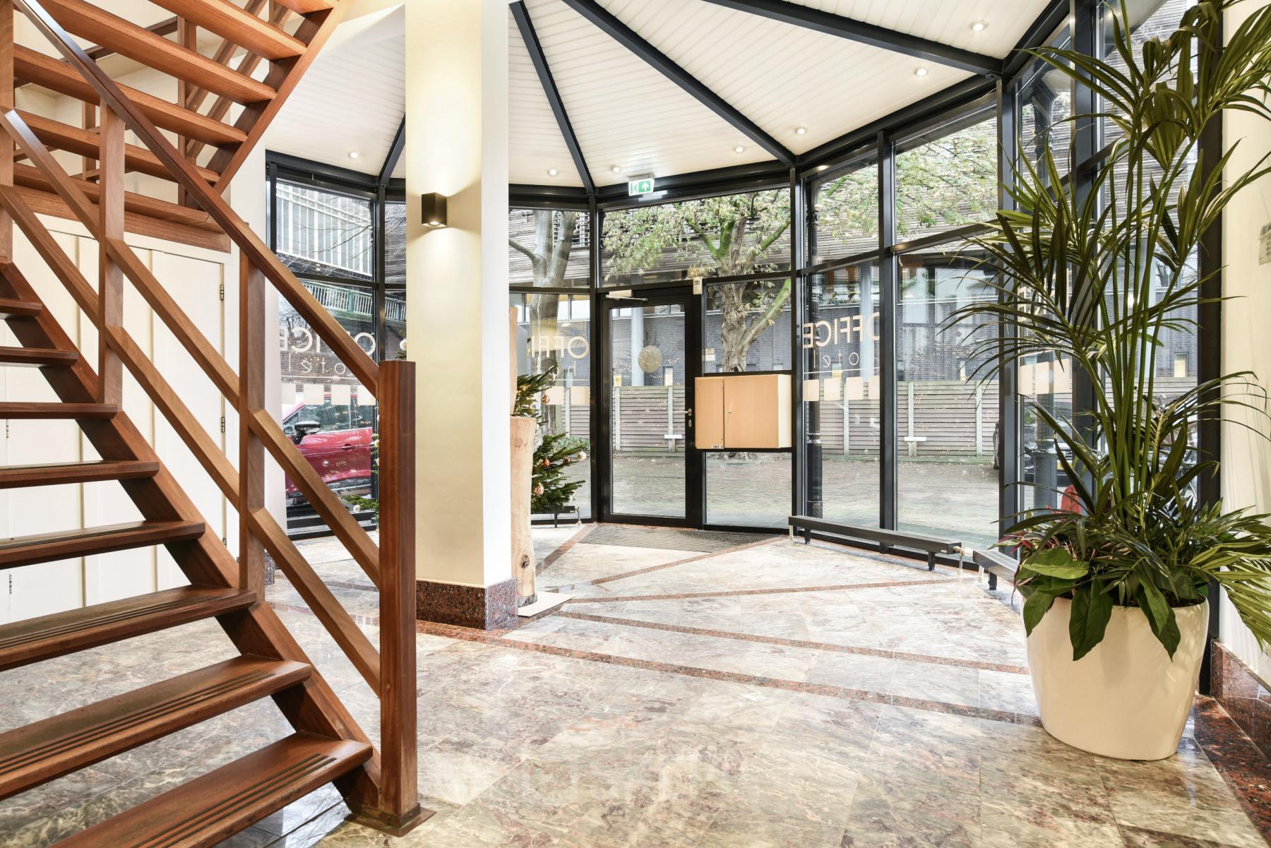 Moderne entreehal van een kantoorpand op Kennemerplein 20, met hoge glazen wanden, marmeren vloeren en een stijlvolle houten trap.