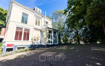 Gevel van een karakteristiek kantoorpand te huur aan het Prinsen Bolwerk 1 in Haarlem, nabij Centraal Station, omgeven door groen met een klassieke uitstraling.