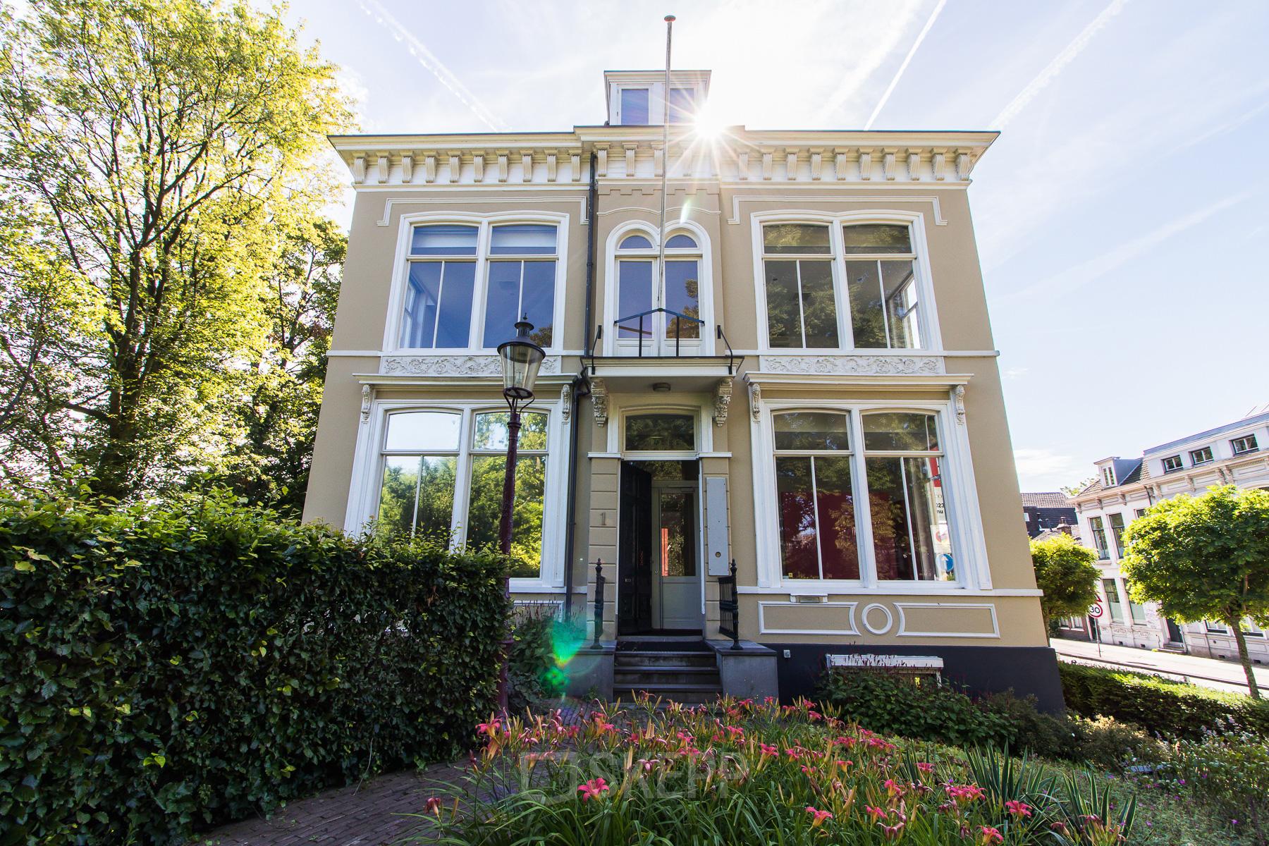 Kantoorpand op Prinsen Bolwerk 1 in Haarlem Centraal Station, omgeven door groene struiken en hier en daar bloemen, onder een heldere lucht.