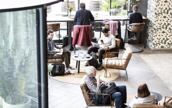 Kantoorruimte huren bij Haarlem Centraal Station, Kennemerplein 6-14, Haarlem. Mensen werken geconcentreerd aan laptops in een moderne ingerichte werkruimte met comfortabele zitplaatsen en een grote glazen wand.