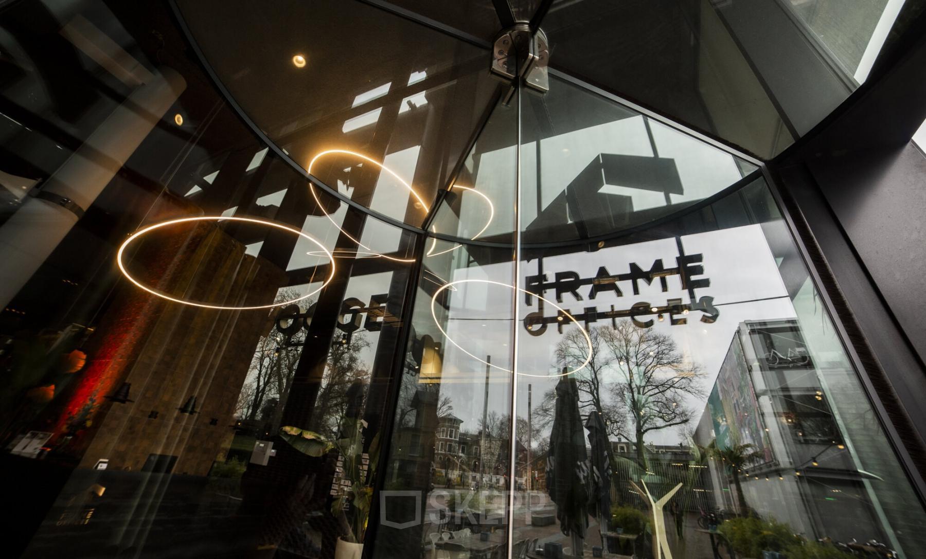 Revolverende glazen deur van kantoorpand Kennemerplein 6-14, Haarlem Centraal Station, weerspiegelingen van de straat zichtbaar in de ramen. Kantoorruimte huren met moderne uitstraling.