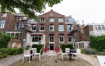 Achtertuin van kantoorpand op Nieuwe Gracht 3 in Haarlem Centrum, met verschillende stoelen en tafels buiten, en een groot bakstenen gebouw met rode kozijnen.