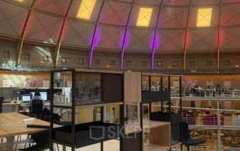 Moderne werkruimte in kantoorpand op Koepelplein 1E, Haarlem Centrum, met open vloerplan en stijlvolle meubels. Mensen aan het werk aan bureaus in de lichte, ruime omgeving met kleurrijke dakkoepel.