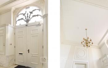 Ingang van het kantoorpand op Nieuwe Gracht 74-76, Haarlem Centrum; klassieke deur met boogvormig raam erboven, witte muren en een sierlijke kroonluchter aan het plafond.