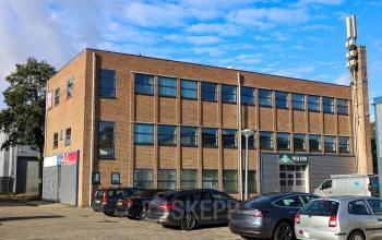 Bakstenen kantoorpand gelegen aan Nijverheidsweg 50 in Haarlem Oost met parkeerruimte aan de voorzijde. Ideaal voor kantoorruimte huren. Heldere blauwe lucht zichtbaar.