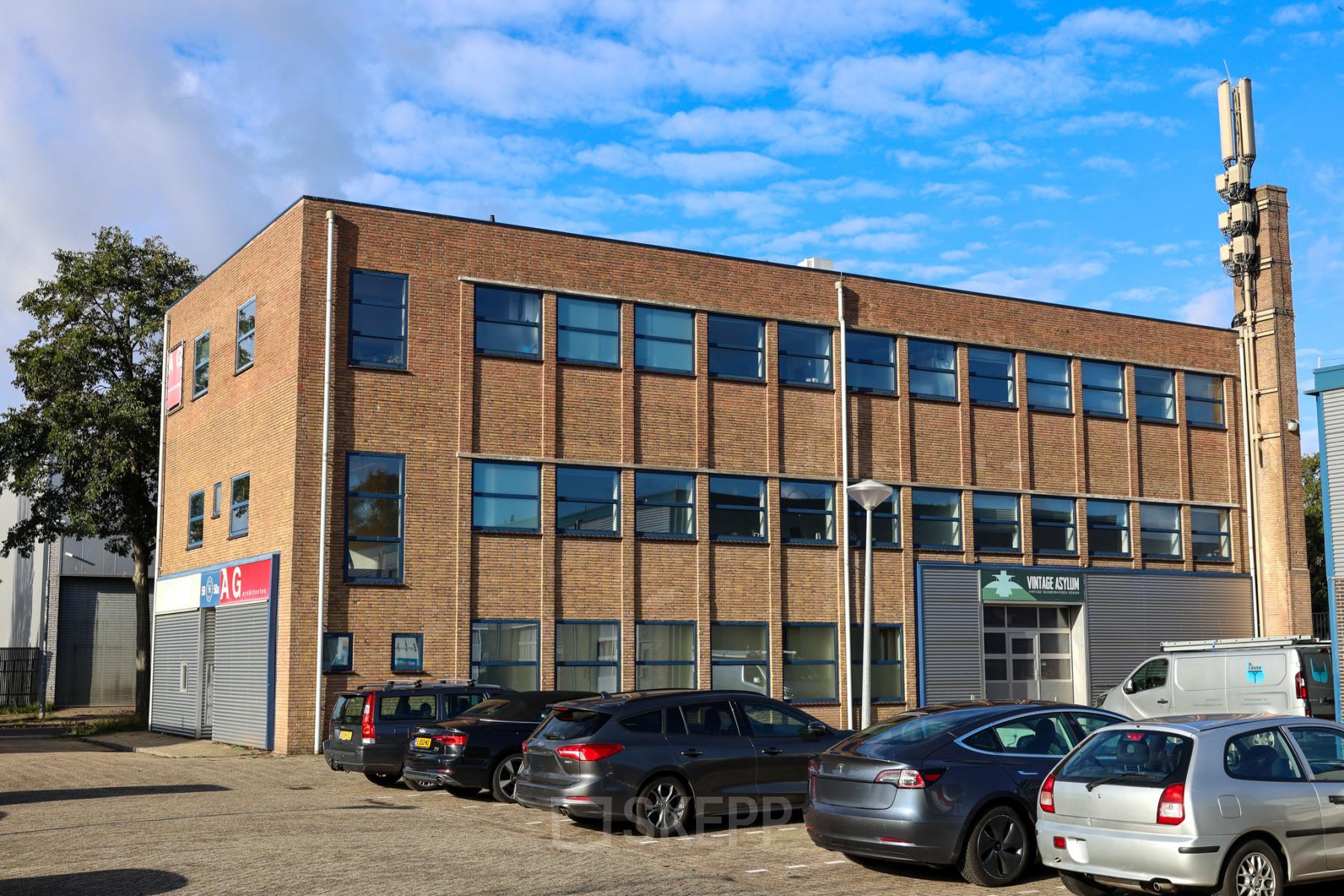 Bakstenen kantoorpand gelegen aan Nijverheidsweg 50 in Haarlem Oost met parkeerruimte aan de voorzijde. Ideaal voor kantoorruimte huren. Heldere blauwe lucht zichtbaar.