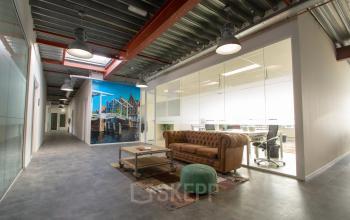 Kantoorpand aan Bingerweg 18A-18R in Haarlem Waarderpolder met moderne glazen wanden en een uitnodigende lounge met bruine leren bank en kleurrijk tapijt. Perfect om kantoorruimte te huren.