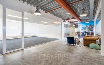 Ruime kantoorruimte met glazen wanden en een betonnen plafond, met een houten vloer en enkele fauteuils. Ideaal voor kantoorruimte huren in de Waarderpolder, Haarlem.