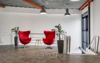 Lichte kantoorruimte in kantoorpand Haarlem Waarderpolder met twee moderne rode stoelen en planten, perfecte plek voor een informele vergadering of pauze.