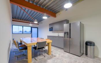 Functionele pantry bij kantoorpand op Bingerweg 18A - 18R in Haarlem Waarderpolder, voorzien van grote houten tafel, stoelen, grijze kasten en moderne koelkast in lichte ruimte geschikt voor kantoorruimte huren.