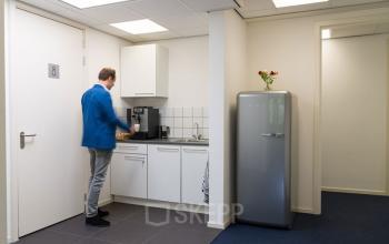Een bescheiden pantry in een kantoorpand aan de Waarderweg 33 in Haarlem Waarderpolder. Een persoon in blauwe jas gebruikt het koffiezetapparaat. Ideale plek voor een werkpauze.