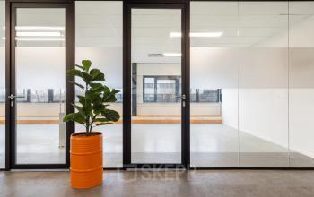 Kantoorruimte huren op Waarderweg 52 in Haarlem Waarderpolder met glazen wanden en een oranje bloempot in een lichte ruimte.