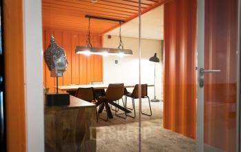 Moderne kantoorruimte huren in Haarlem Waarderpolder met glazen deur, stoere oranje muren en vergadertafel met stoelen, ideaal voor team meetings of creatieve sessies.