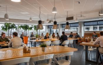 Kantoorruimte huren in een licht en gemeubileerd kantoorpand op A. Hofmanweg 5A, Haarlem Waarderpolder. Personen vergaderen en werken aan grote tafels in een open werkruimte.