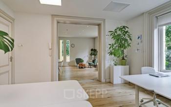 Binnenzicht van kantoorpand Florapark 7 in Haarlem Zuid. Lichte ruimte met houten vloer, bureaus en grote planten. Enkele mensen werken in de verte.