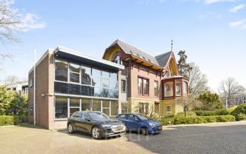 Kantoorpand Florapark 7 in Haarlem Zuid, Haarlem. Uitbreiding met moderne glazen gevel en auto's geparkeerd voor het gebouw. Mogelijkheid tot kantoorruimte huren.