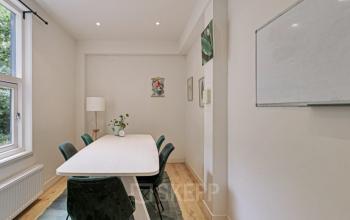 Kantoorruimte huren in een moderne vergaderruimte met een lange tafel, zes groene stoelen, een witte lamp en schilderijen aan de muur, gelegen in het kantoorpand op Florapark 7, Haarlem Zuid, Haarlem.