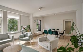 Lichte, gemeubileerde kantoorruimte met grote ramen, comfortabele zitbanken en groene planten in het kantoorpand op Florapark 7, Haarlem Zuid, Haarlem.